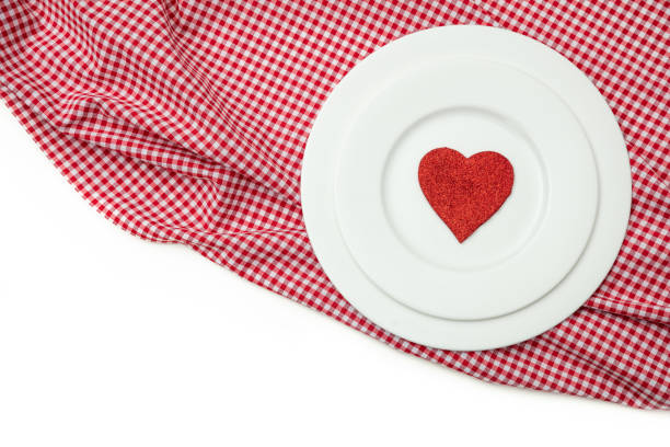Valentines day dinner, table, place setting. Red heart on white plates, red checkered table cloth, white background, copy space, top view.