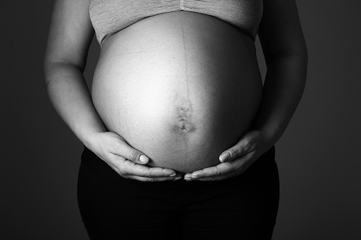 Pregnant women holding hands on abdomen side view studio shot