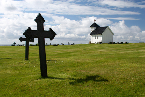 Warm summer sunlight bathes the central entrance of the traditional, wooden Kvam Church in Nord-Fron, Norway, nestled amidst a well-maintained cemetery with gravestones