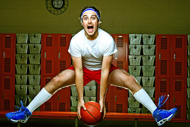 Male Basketball Player Jumping Around in Locker Room with Ball young baller in the locker room getting read for the game legs apart stock pictures, royalty-free photos & images