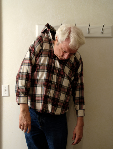 Color vertical of a male senior citizen hanging by his shirt collar on a wall hook.