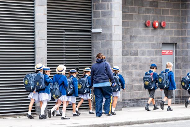 Group of many school children on field trip walking on sidewalk street with uniforms, backpacks and teachers guardians in Westminster, Pimlico London, UK - September 12, 2018: Group of many school children on field trip walking on sidewalk street with uniforms, backpacks and teachers guardians in Westminster, Pimlico london girl stock pictures, royalty-free photos & images