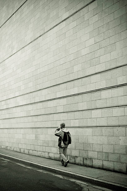 Young Man Walking on Sidewalk Against Concrete Block Wall