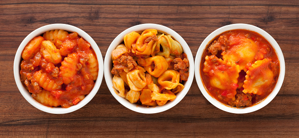 Top view of three white bowls with varieties of pasta bolognese in them (gnocchi, tortellini and ravioli)
