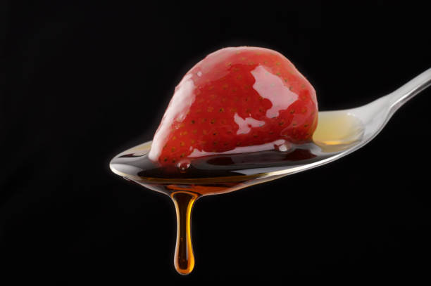 gocciolamento di sciroppo di fragola su un cucchiaio - honey caramel syrup fruit foto e immagini stock