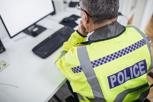 One senior traffic warden sitting at the office in front of the computer and writing a report