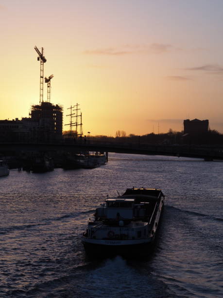 Bremen, Germany - December 11th, 2018 - Cargo ship on the river Weser at sunrise with construction site and cranes in the distance