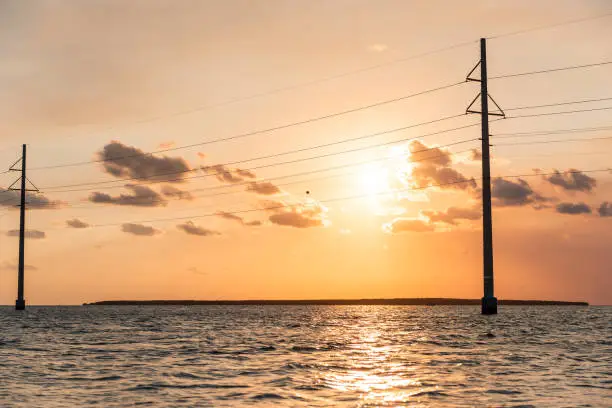 Sunset in Islamorada, Florida Keys, with orange vintage dreamy pink sky, power lines, water on gulf of Mexico, or Atlantic Ocean, horizon with sun behind clouds, island