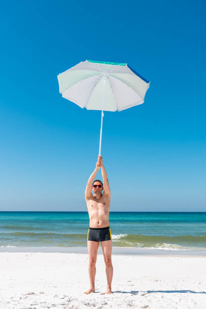 giovane uomo muscoloso in forma felice sorridente divertente sulla spiaggia durante la giornata di sole con occhiali da sole rossi in florida panhandle con vista verticale, oceano, ombrellone - umbrella beach sex symbol white foto e immagini stock