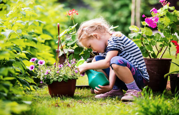 cute little girl watering plants in the garden - spring child green small imagens e fotografias de stock
