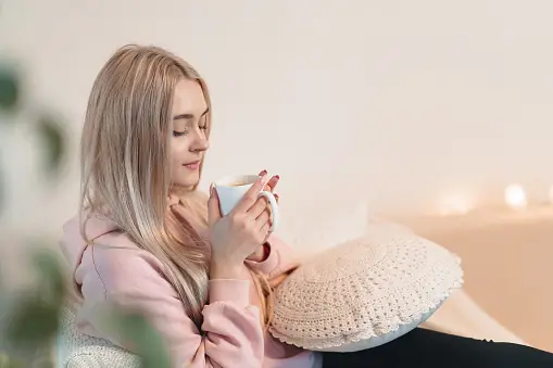 Thoughtful young woman sitting on sofa with a cup of milk, coffe