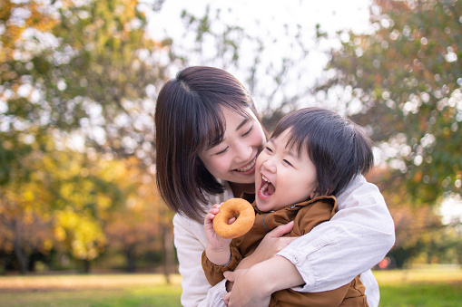 Young mother and son eating doughnut in public park with full of fun