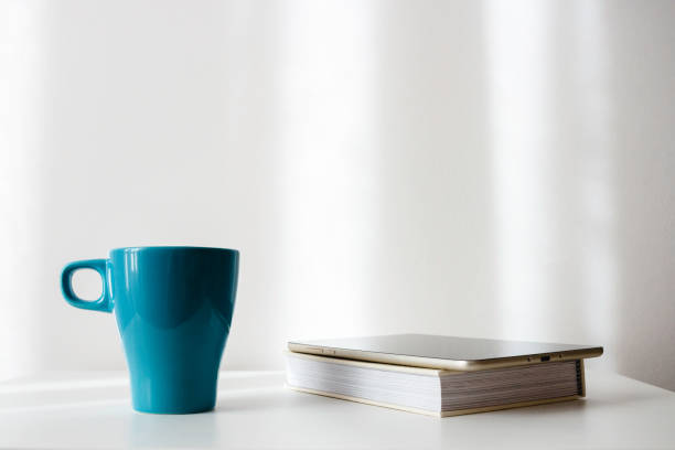 Tablet, paper book and cup in light cozy interior