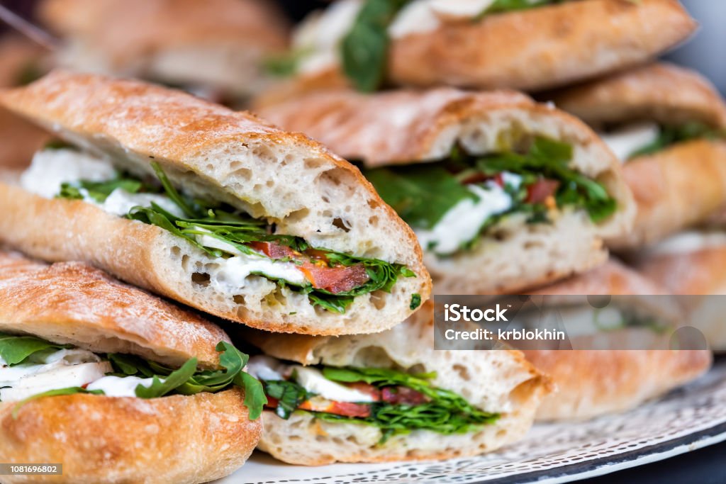 Closeup of fresh display of stacked pile of panini bread, mozzarella melted cheese, vegetarian italian tomatoes, basil lettuce in store, shop, cafe buffet catering sandwiches Sandwich Stock Photo