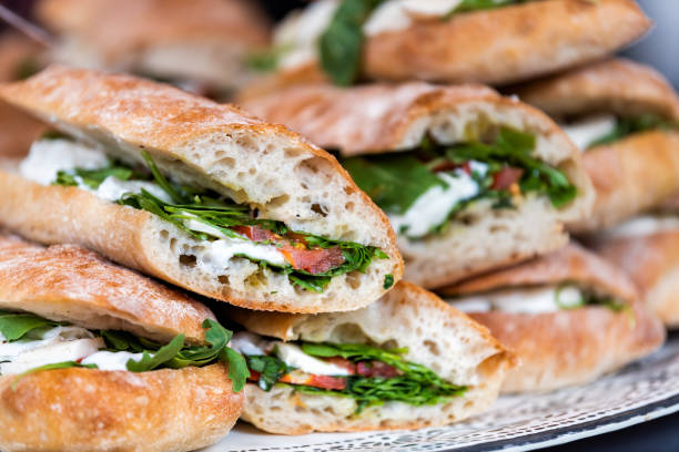 closeup of fresh display of stacked pile of panini bread, mozzarella melted cheese, vegetarian italian tomatoes, basil lettuce in store, shop, cafe buffet catering sandwiches - sandwich delicatessen bread cheese imagens e fotografias de stock
