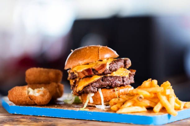 burger greasy stacked street food, fried french fries closeup, melted cheese and bun on blue tray display in restaurant closeup, breaded fish sticks, bacon - bacon cheeseburger imagens e fotografias de stock