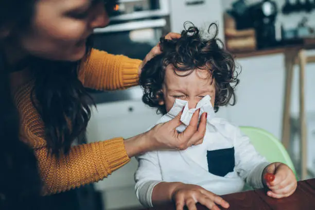 Mother helping son to blow his nose at home