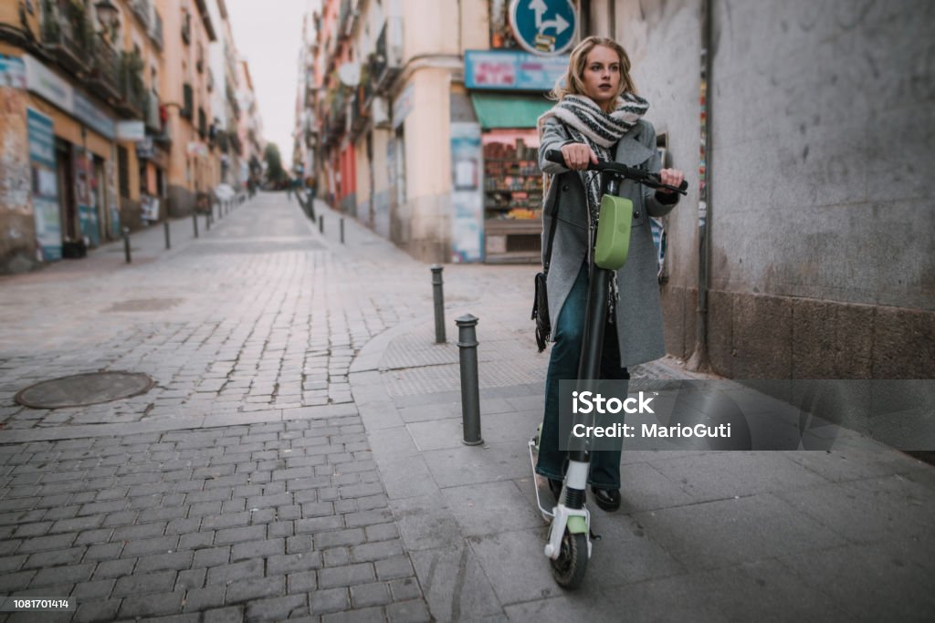 Young woman riding an electric scooter in a city A young woman in a street, riding an electric scooter Electric Vehicle Stock Photo