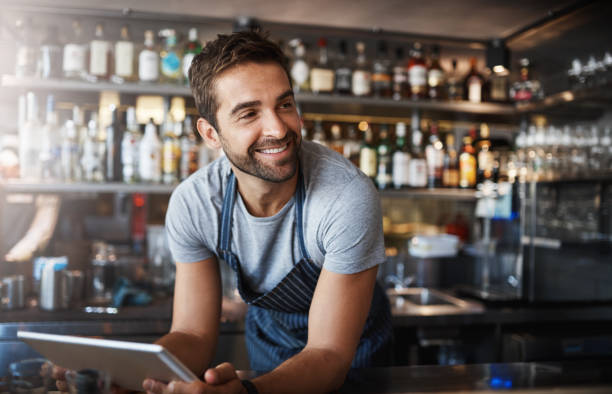 The bar has never been better Shot of a young man using a digital tablet while working behind a bar counter cafe tablet stock pictures, royalty-free photos & images