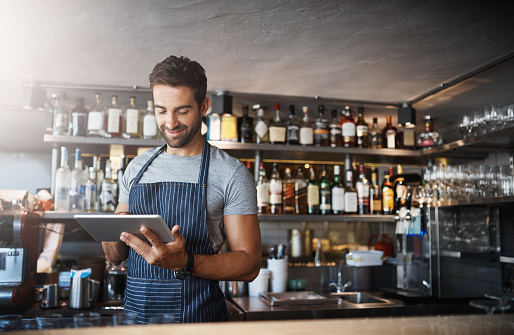 Shot of a young man using a digital tablet while working behind a bar counter