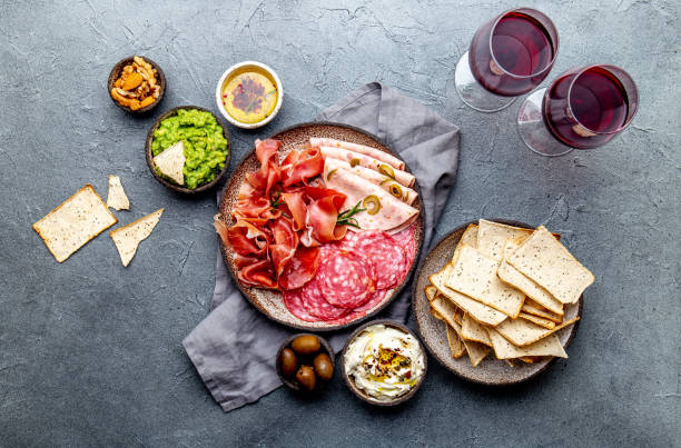 antipasto. piatto di carne, patatine e salse, vino rosso su sfondo grigio. visualizzazione dall'alto - salami prosciutto italian culture food foto e immagini stock