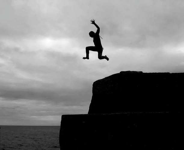 A young man is in midair having jumped off a pier into the sea