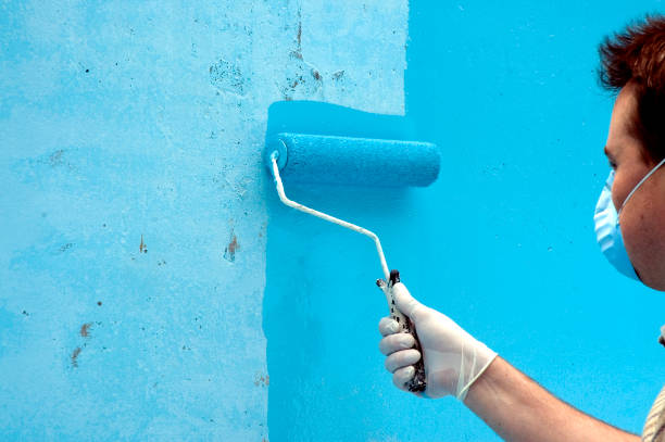 Painter wearing face mask while painting a wall bright blue stock photo