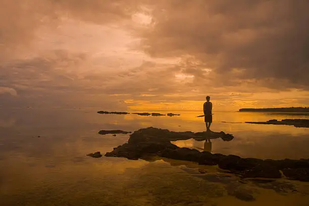 Photo of Sunset Silhouette of Man Standing on Rocks Near Calm Water