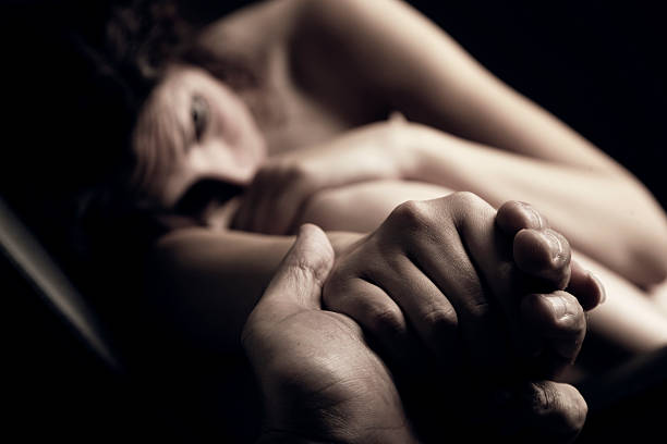 Man Holding Naked and Crouching Woman's Hand Focus on two holding hands. Naked crouching girl in the background. self mutilation pictures stock pictures, royalty-free photos & images
