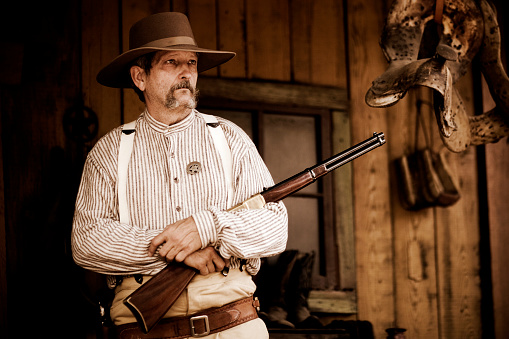 wide angle, close up shot of a guy dress as an american cowboy, aiming his revolver up