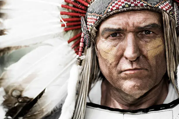 Horizontal portrait of a Native American Chief wearing a feathered head dress.