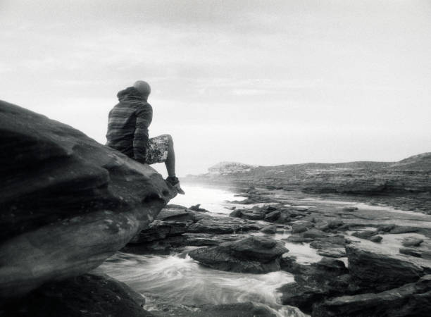 istock Young Man Sitting on Rock Watching Tide, Black and White 108175839