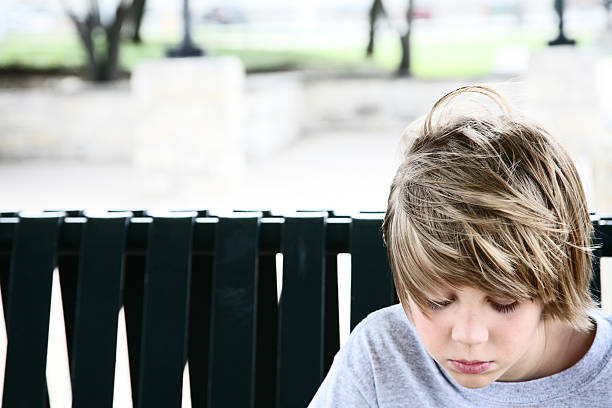 Young boy sitting on a bench at the train station, waiting.