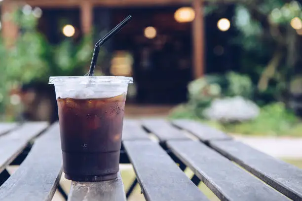 Photo of A plastic cup of iced Americano (black coffee) serving on the wood plank table.