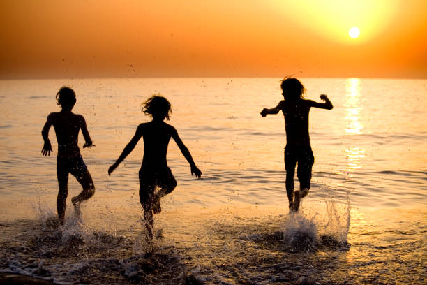 istock Three kids jumping and splashing in the water at sunset 108176308
