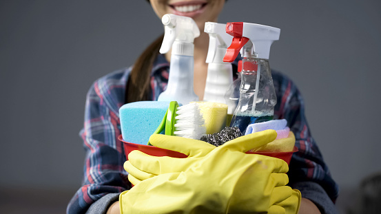 Smiling woman lifting up bucket with numerous household cleaning substances