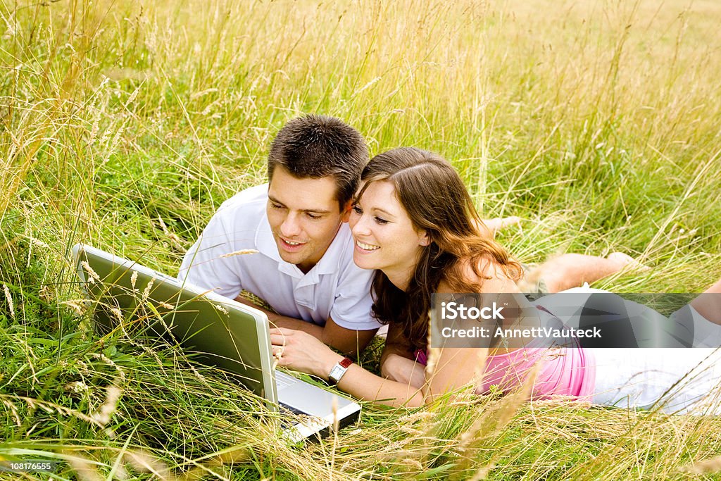 Casal feliz deitado na Meadow olhando para Laptop - Foto de stock de 20 Anos royalty-free