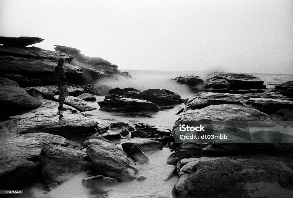 若い男性の上に立つ海岸沿いのロック、ブラックおよびホワイト - オーストラリアのロイヤリティフリーストックフォト