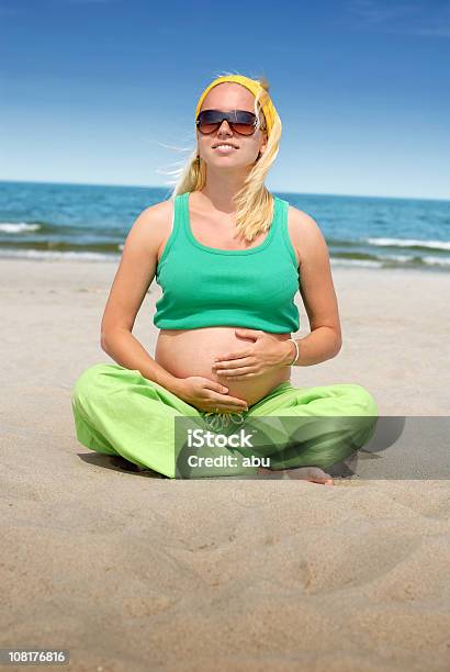 Беременная Женщина Сидя На Пляже Держа Мышцы Живота — стоковые фотографии и другие картинки Беременная