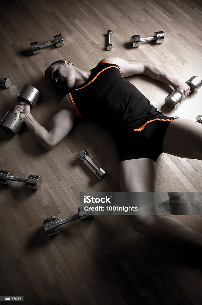 Esaurito uomo si trova sul pavimento circondato da Barbells e pesi - Foto stock royalty-free di Argento
