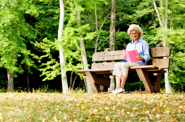 istock Senior Woman Sitting On A Park Bench Reading 108177216