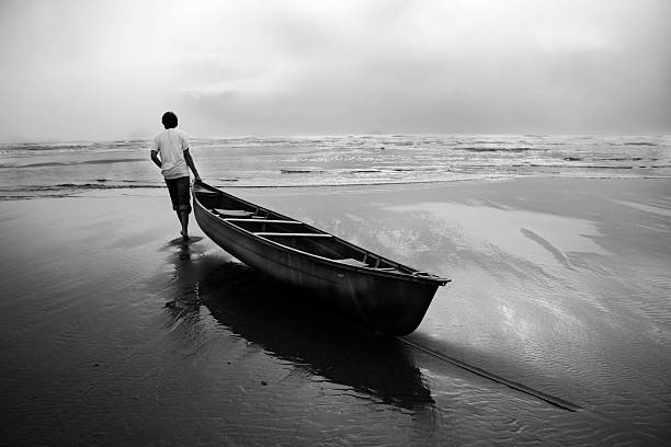 Man Dragging Canoe Boat into Ocean, Black and White  dragging photos stock pictures, royalty-free photos & images