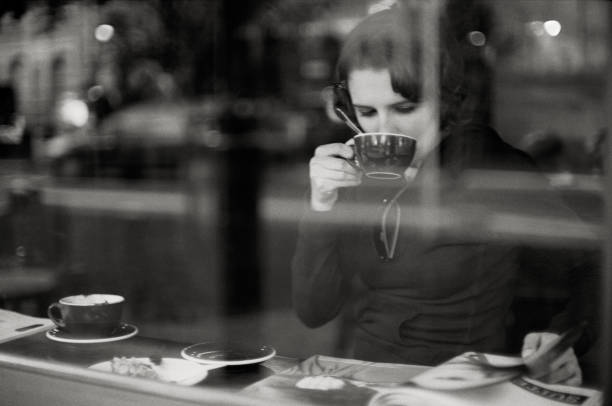 Woman drinking coffee and reading magazine behind window