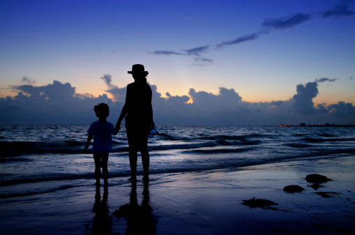 Albion, Mauritius - May 01, 2023: People standing in the Indian Ocean watching the vibrant colors during a sunset in Albion in the West of Mauritius.