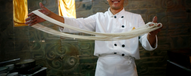 Chef showing off hand stretched noodles made from a traditional dough.