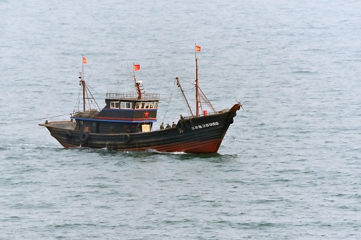 Scarborough, UK.  February 19, 2024.  Three fishing boats moored in harbour. A path with wooden posts and chains leads down to the water’s edge.