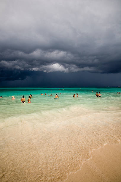 A tropical storm forming in the distance at Playa del Carmen beach in Mexico, with people still enjoying the final moments of sun.\n