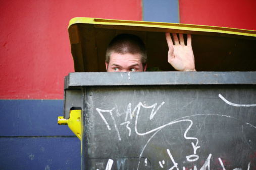 man looking out from trash container.