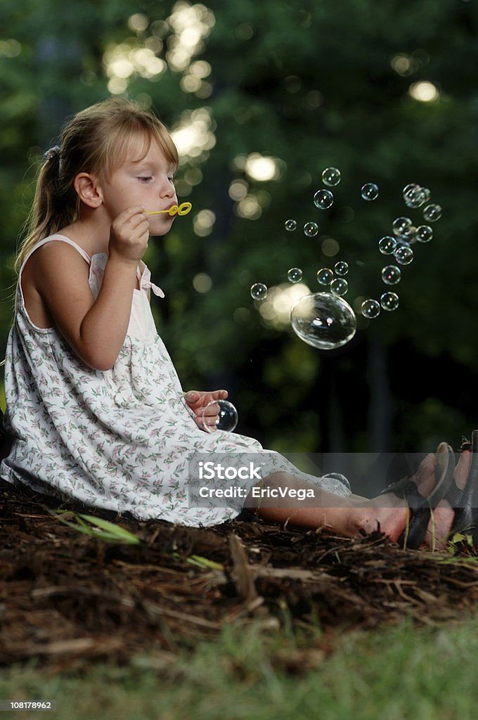 Маленькая девочка, сидящая на траве и послать Bubbles - Стоковые фото В полный рост роялти-фри