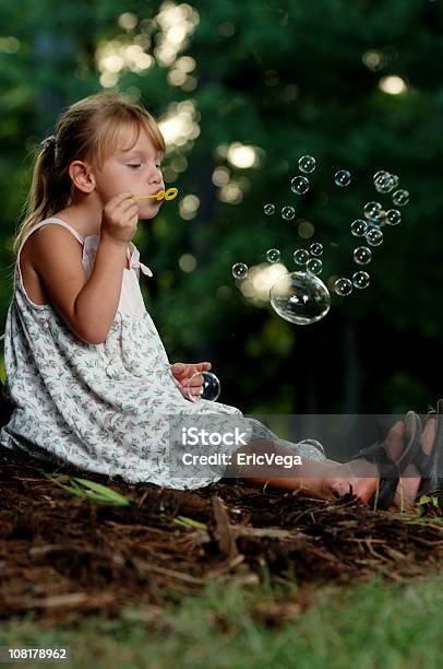 Маленькая Девочка Сидящая На Траве И Послать Bubbles — стоковые фотографии и другие картинки В полный рост